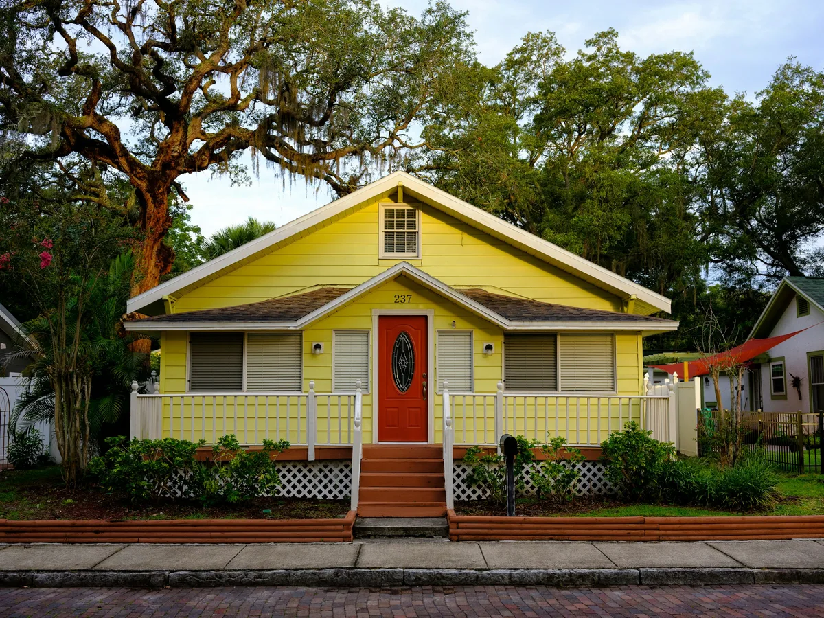A yellow Florida bungalow under a mature live oak, walls and trim clean