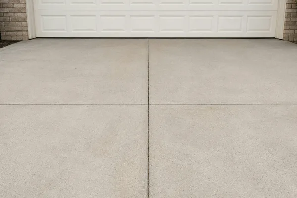 A clean concrete driveway running up to a white garage door.