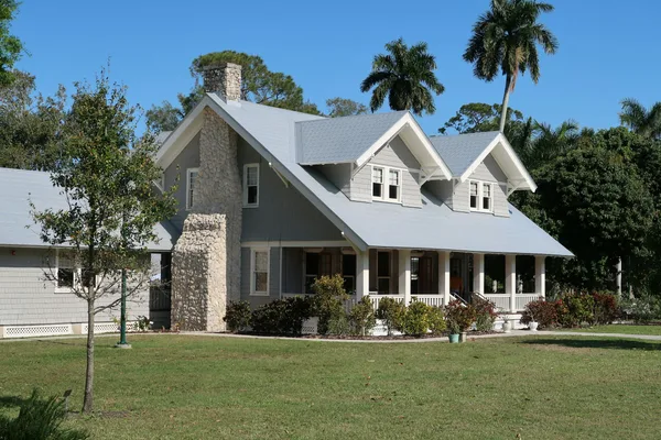 A single story home in Florida with clean siding, a stone porch and palms behind it.
