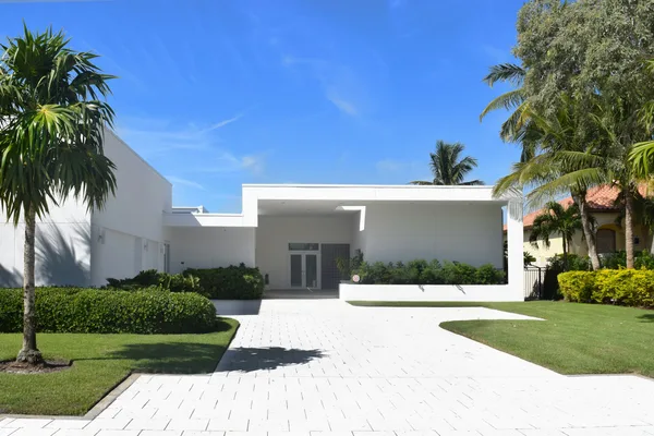A wide paver driveway leading to a low white house under a clear sky.